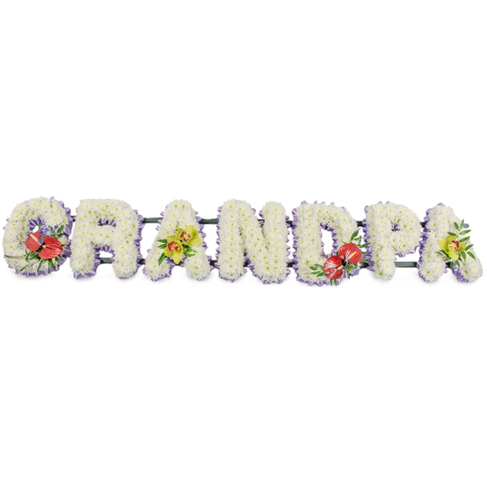 A personalised funeral tribute in the form of the word "GRANDPA" stretches horizontally across a clean, white backdrop, each letter standing tall and distinct yet connected as one loving message. The letters are fully covered with dense clusters of white chrysanthemums, the petite blooms layered and overlapping to form a lush, cushiony texture that looks soft to the touch and radiates a sense of purity and stillness. Around the base of every letter, a fine band of pale lavender ribbon creates a subtle border, its cool lilac tone enhancing the crisp outline and adding just a whisper of colour that feels calm and respectful. The entire word is fixed on a dark green frame, barely visible beneath the masses of petals, lending structure so the tribute can be displayed at a Perivale funeral service, perhaps resting near the altar, by the coffin, or later placed tenderly at a graveside in a nearby cemetery. Four letters carry carefully composed accent sprays that break the white with expressive colour. The opening "G" features deep red anthuriums, their waxy, heart-shaped petals and bold yellow spadices set against dark green leaves, a powerful symbol of affection and enduring love. The first "A" is softened by a cluster of yellow-green orchids, their graceful blooms spilling in a gentle curve over the chrysanthemums, bringing a touch of delicacy and modern elegance. The central "D" repeats the rich red anthuriums, providing visual balance, while the final "A" carries another spray of yellow-green orchids, echoing the earlier accent and suggesting the continuation of cherished memories. Crafted in the thoughtful style of Flower Delivery Perivale, this "GRANDPA" arrangement offers families a quietly beautiful, deeply personal way to honour a much-loved grandfather.